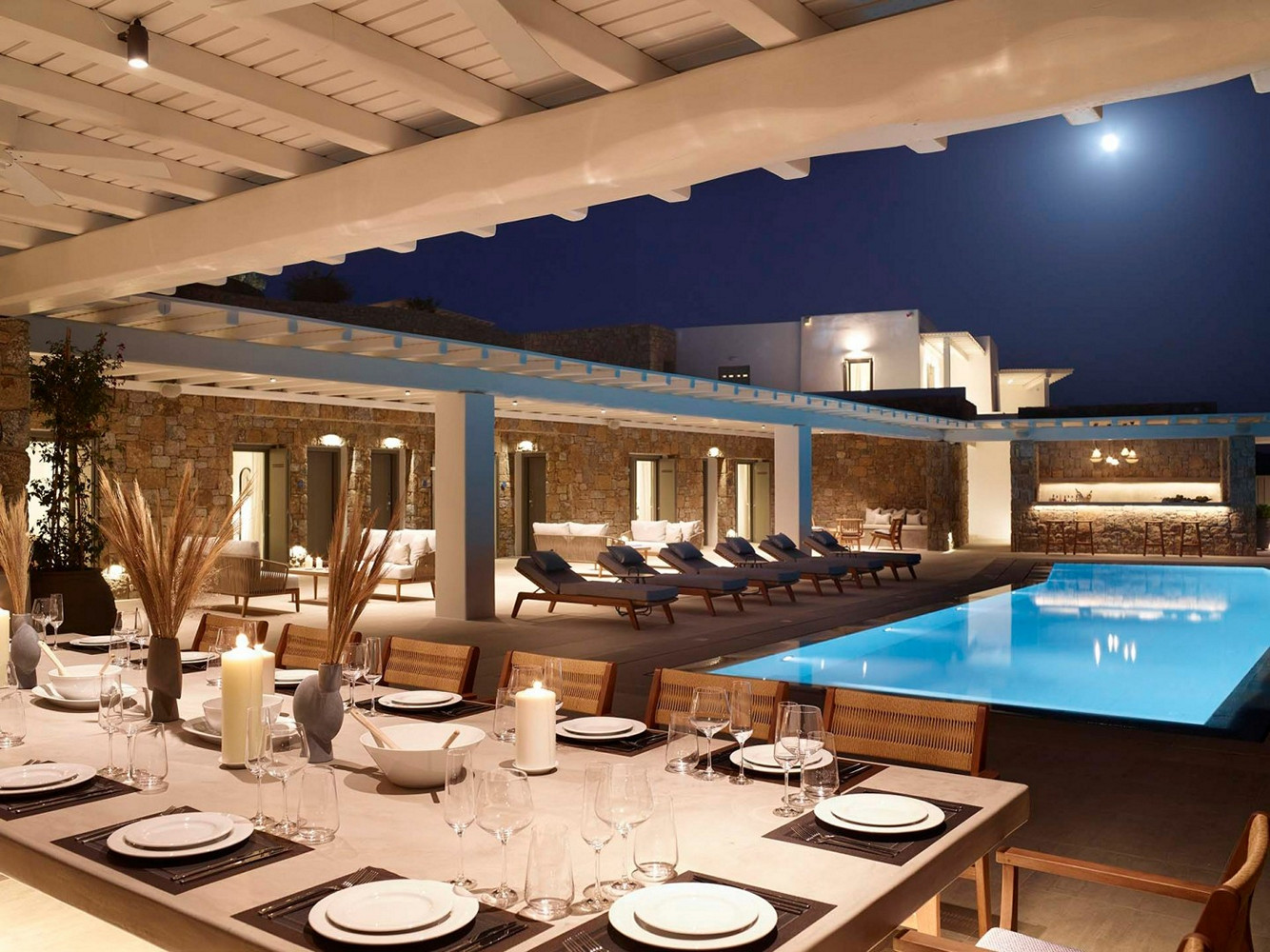 Set dining table and a pool in front of a villa in Mykonos at night 
