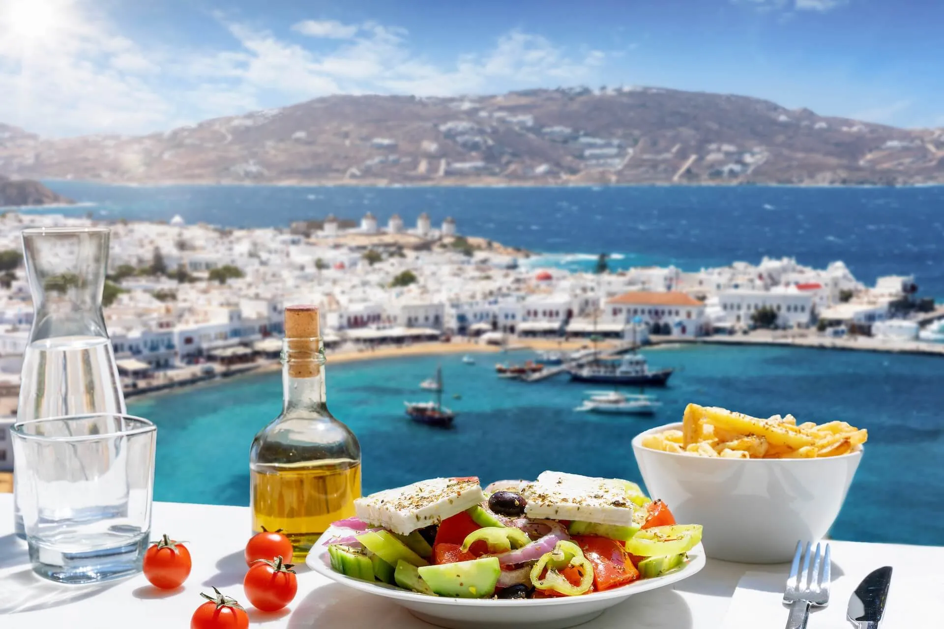 Traditional Greek salad, olive oil, and fries on a table overseeing Mykonos