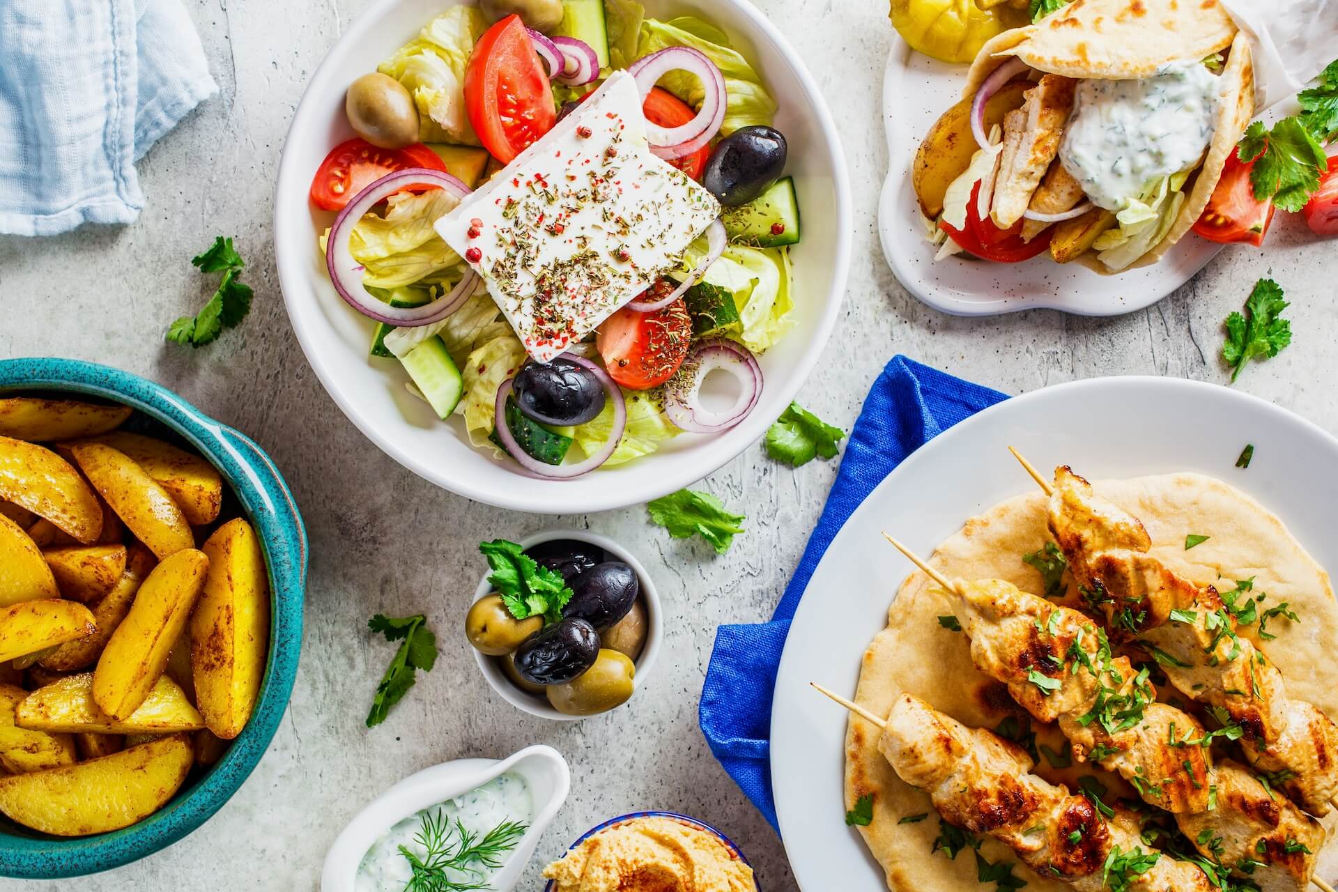 Greek salad, gyros, souvlaki, baked potatoes, and olives on the table 