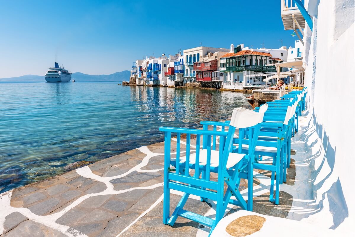 A view of some blue and white chairs, white buildings, and a cruiser on the Aegean Sea
