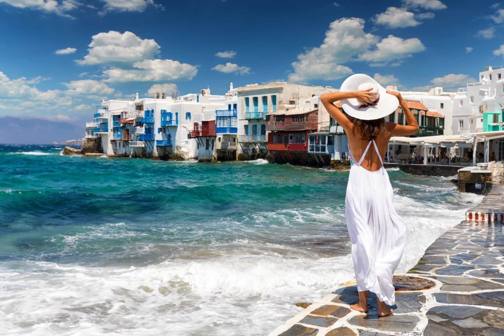 A woman wearing a white dress and white hat, looking at Little Venice on Mykonos