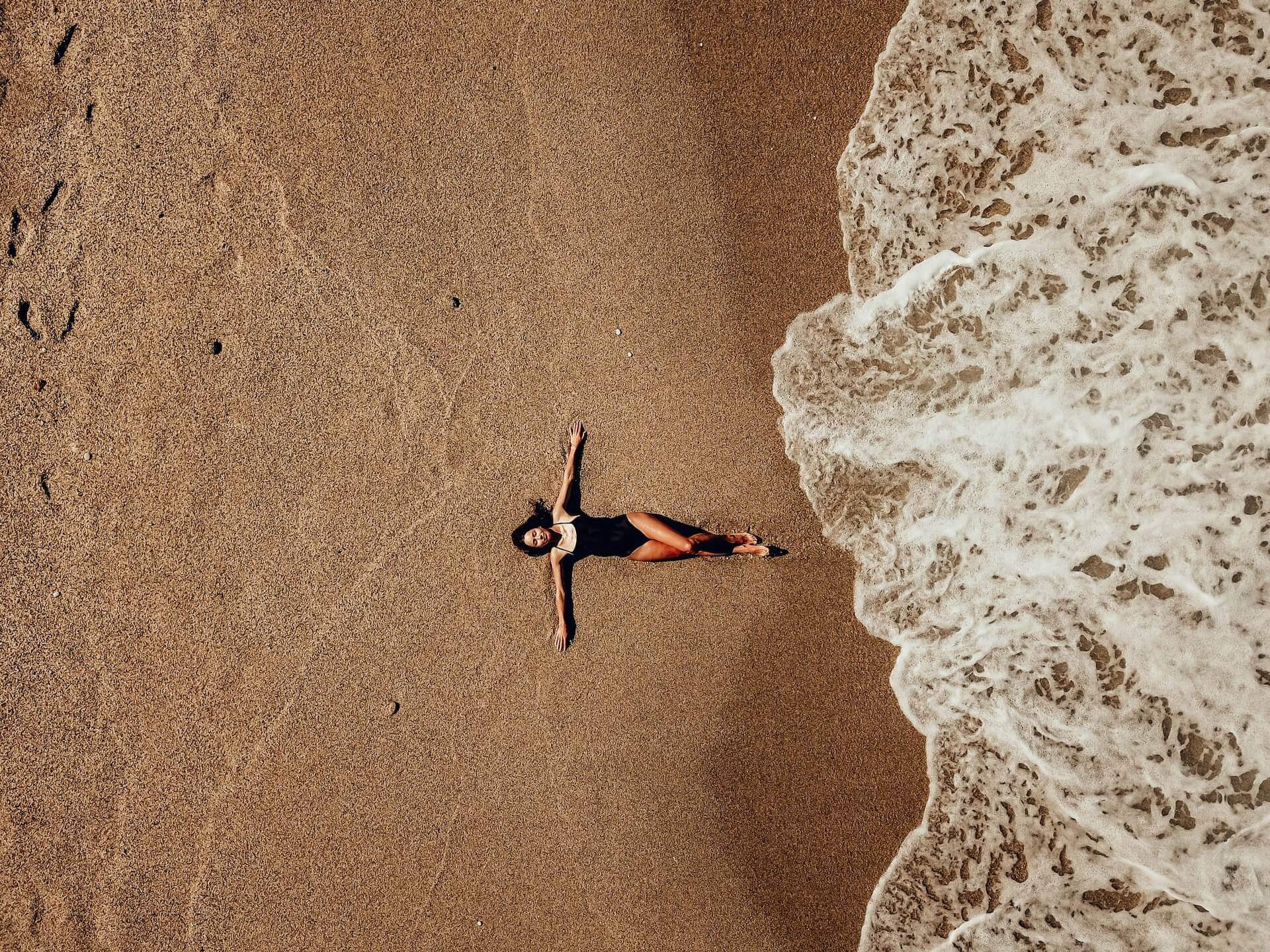 Girl lying on the sand while a wave is approaching