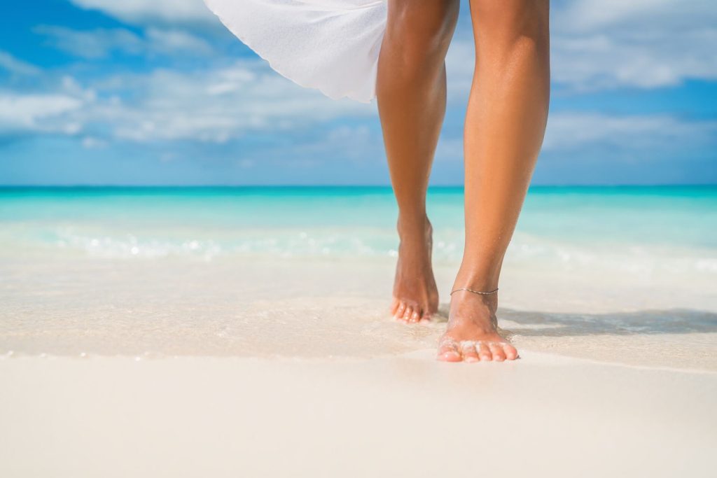 Legs of a woman in a white dress walking on the beach