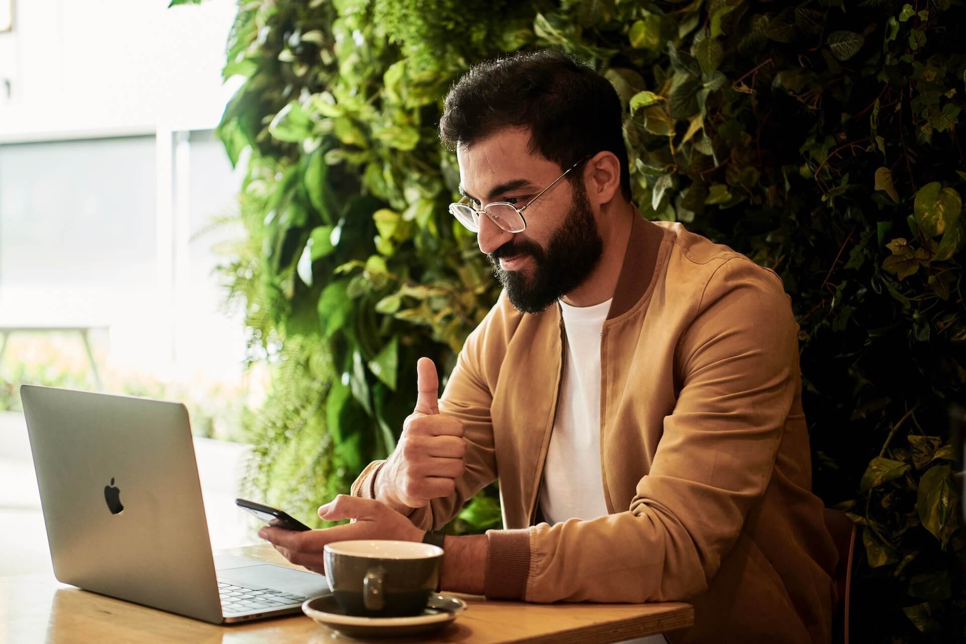  Man looking at the laptop and holding a thumb up, coffee next to him 