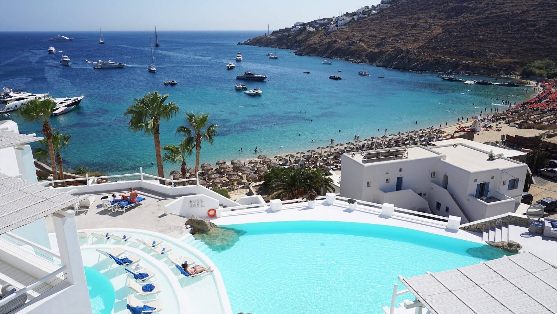 An aerial view of a hotel swimming pool, some swimmers, and the Aegean Sea