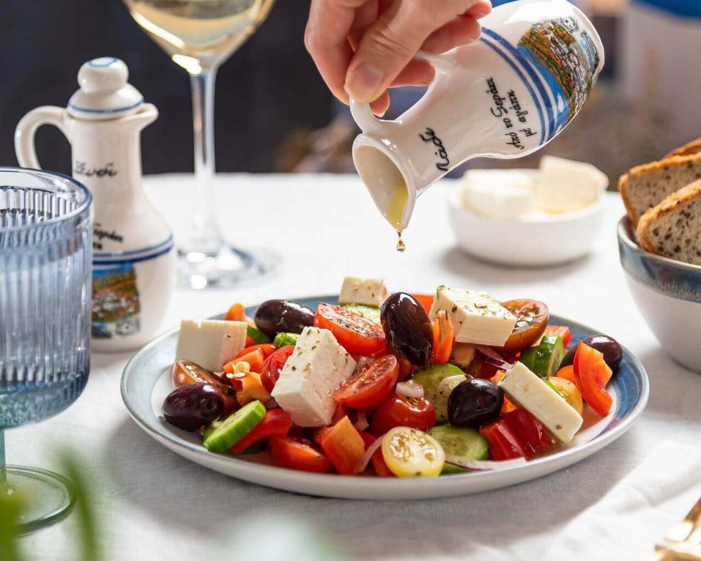 Waiter pouring olive oil over a Greek salad