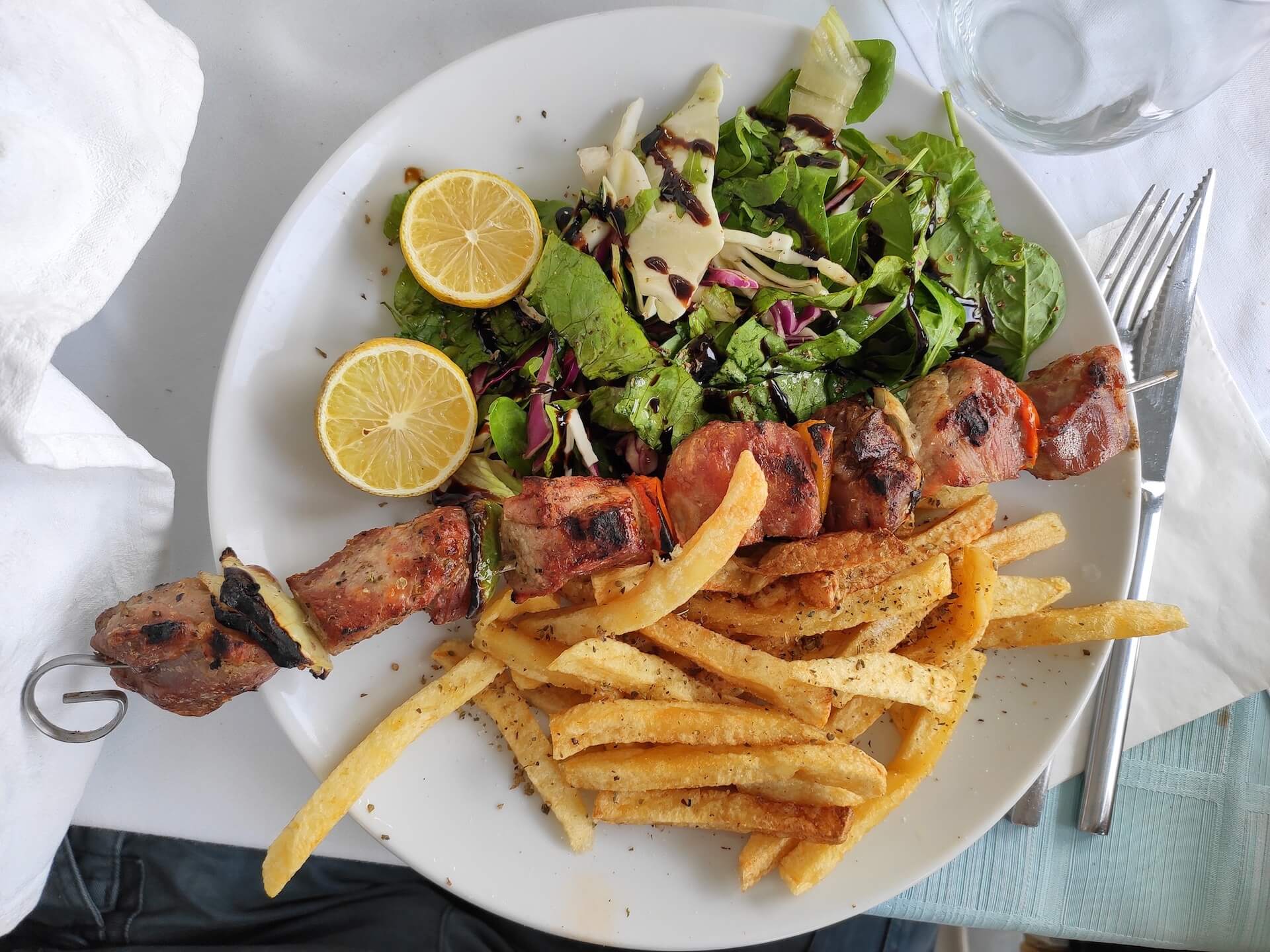 Souvlaki with fries and a salad on a white plate