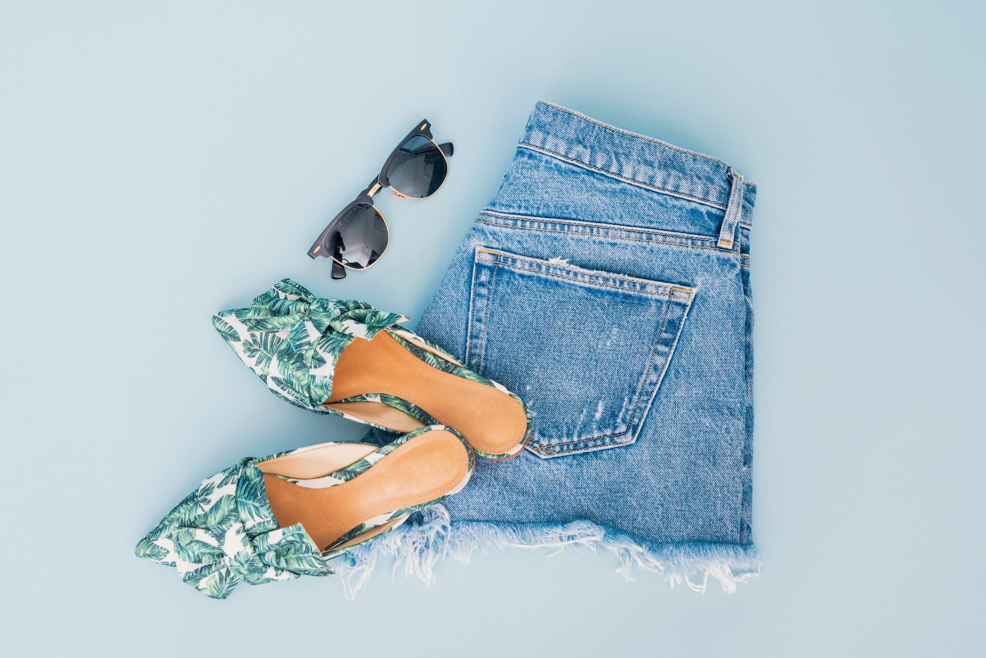 Denim shorts, sunglasses, and sandals on a white surface