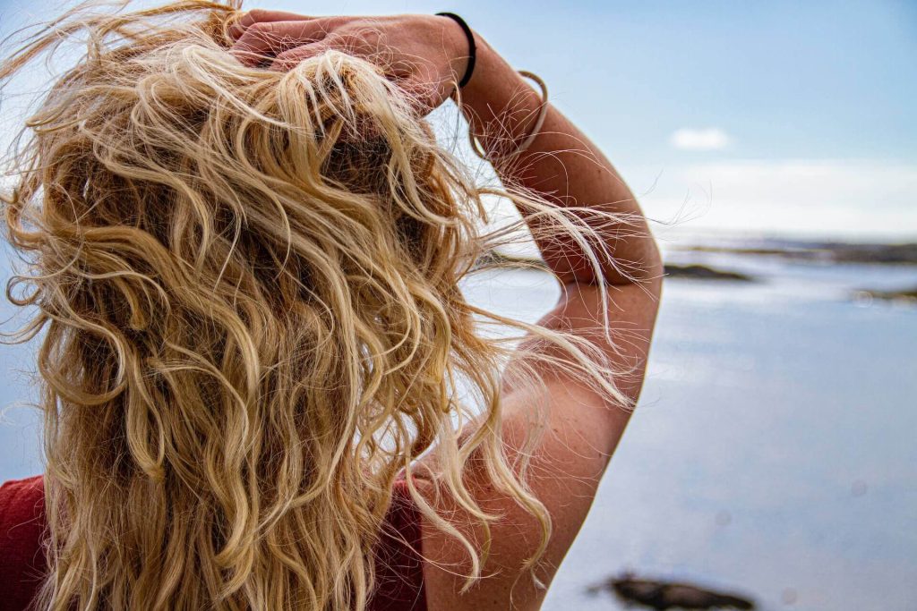 Girl with blonde wavy hair standing next to the sea