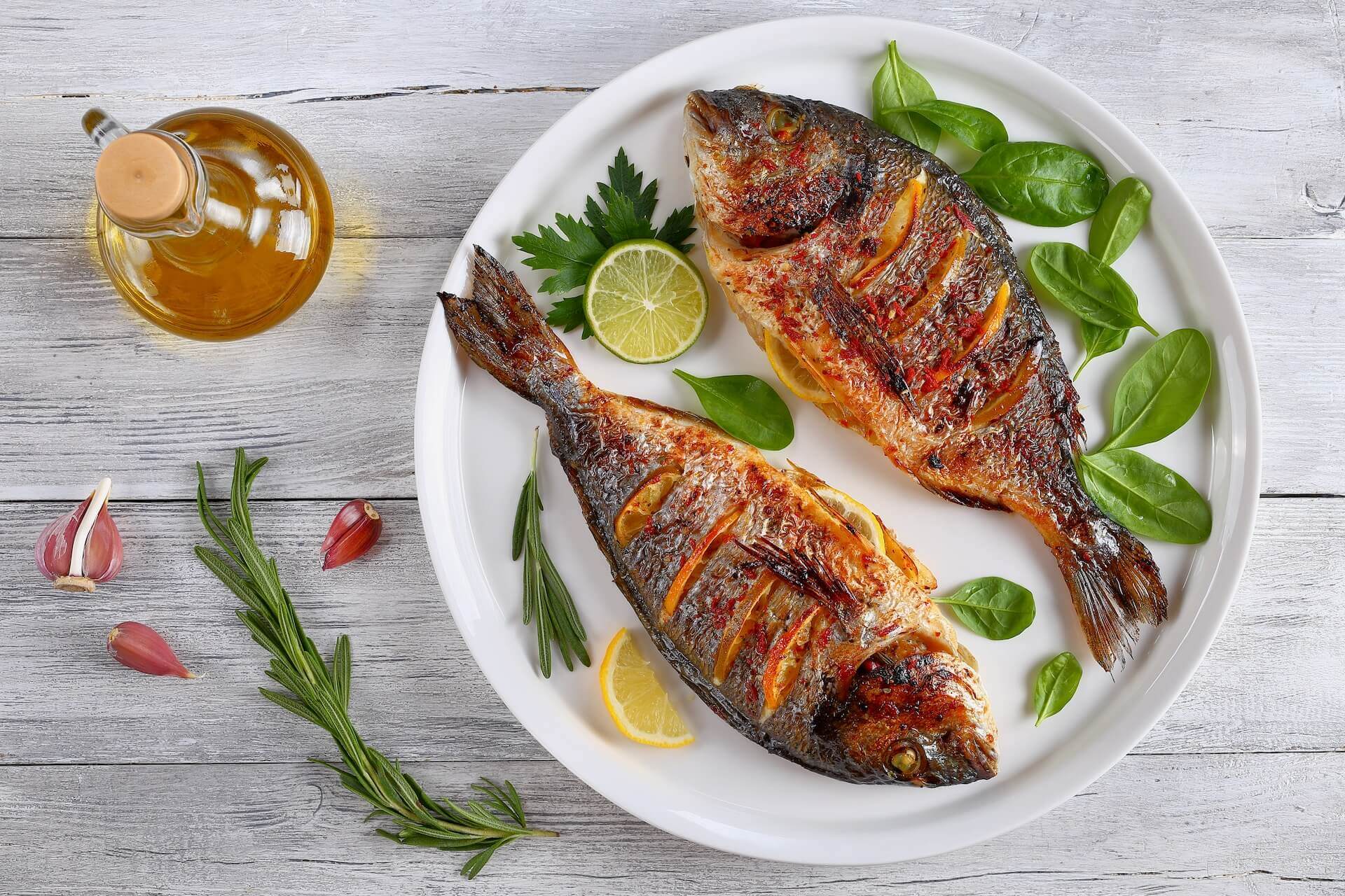 Two grilled fish and lemon slices on the plate, and a bottle of olive oil next to the plate