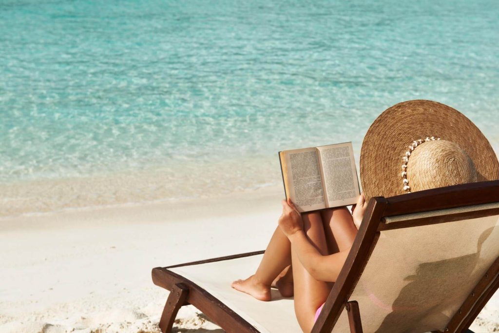 Woman with a hat sitting on a beach in Mykonos and reading a book