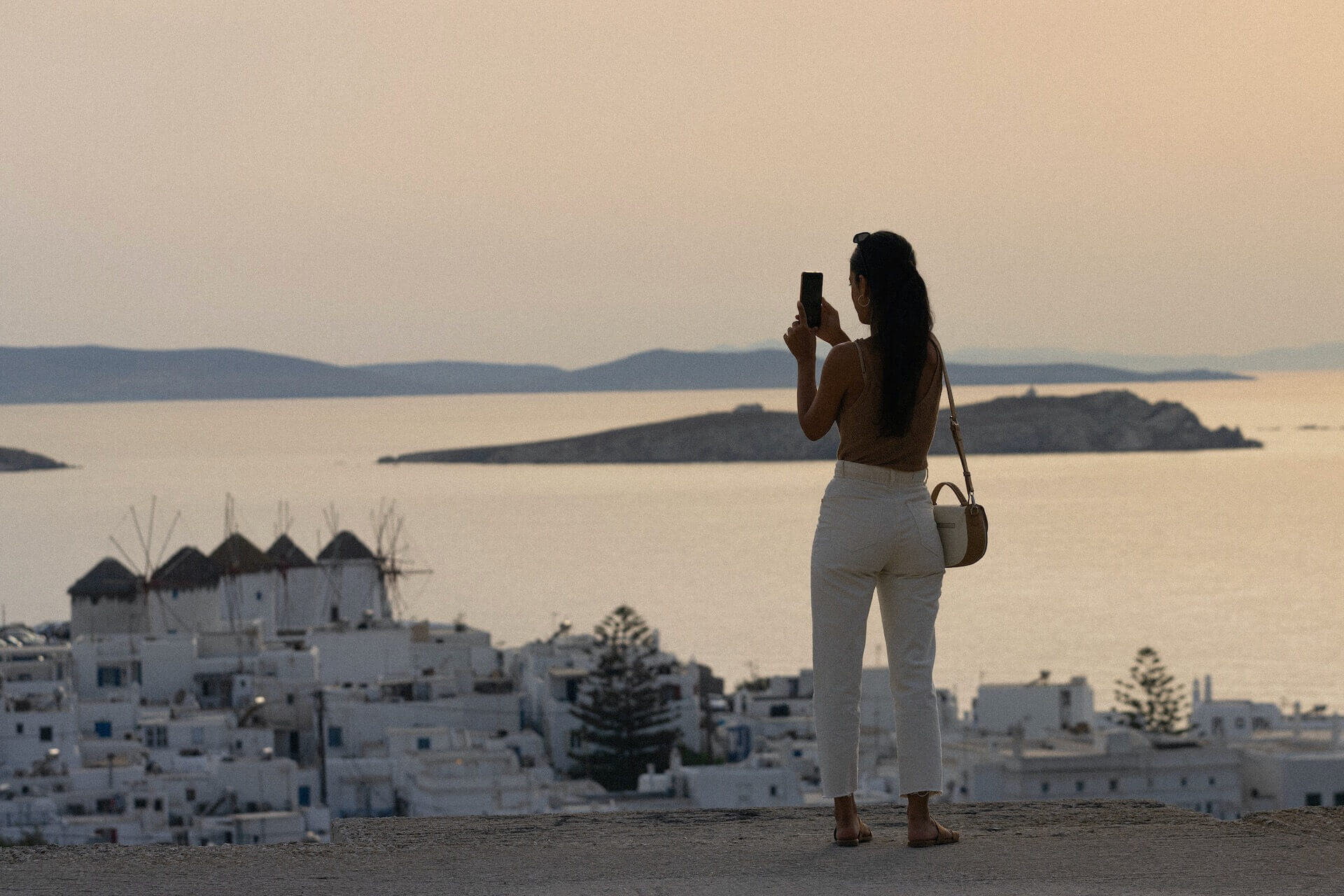 Woman taking a photo of the windmills, standing on the hill in Mykonos town 