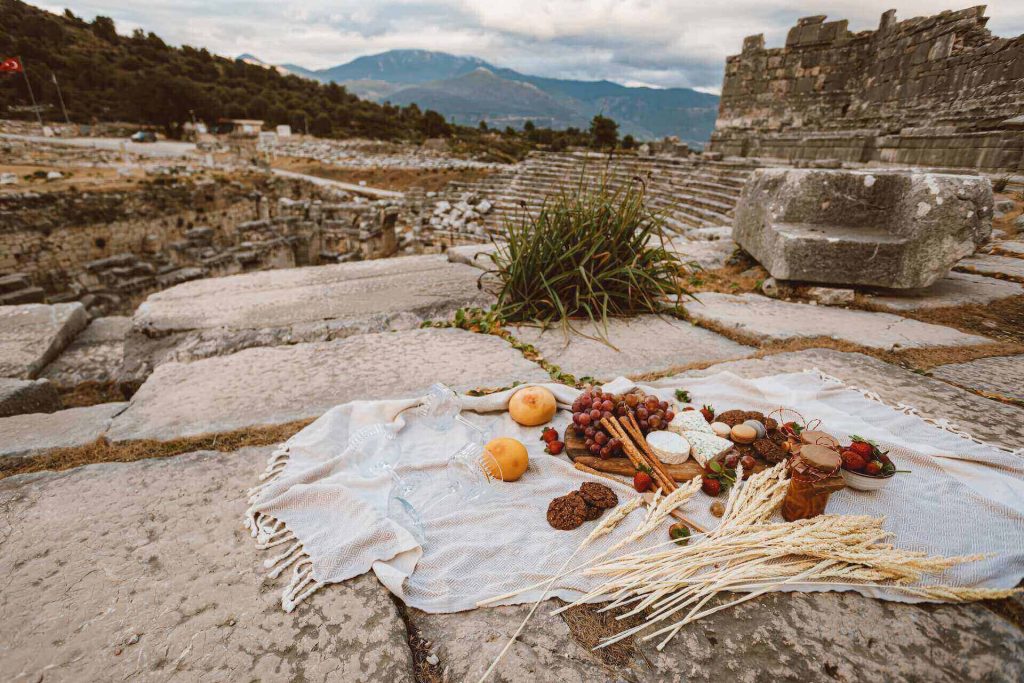 A picnic spread of bread, fruits, and vegetables in ancient ruins