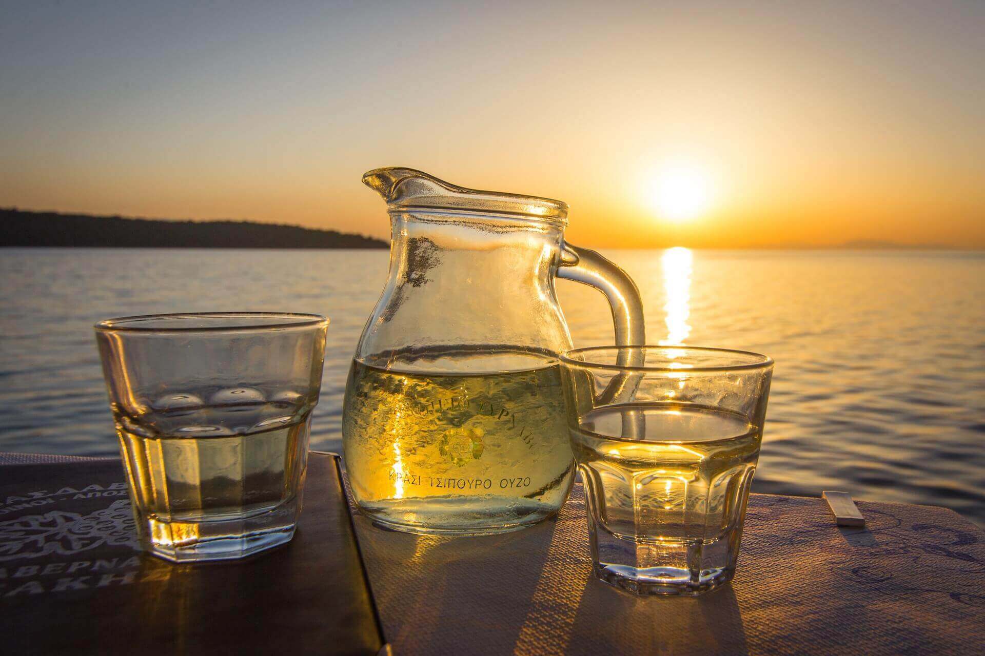 A pitcher of white wine with Greek inscribed on it, and two glasses on the side