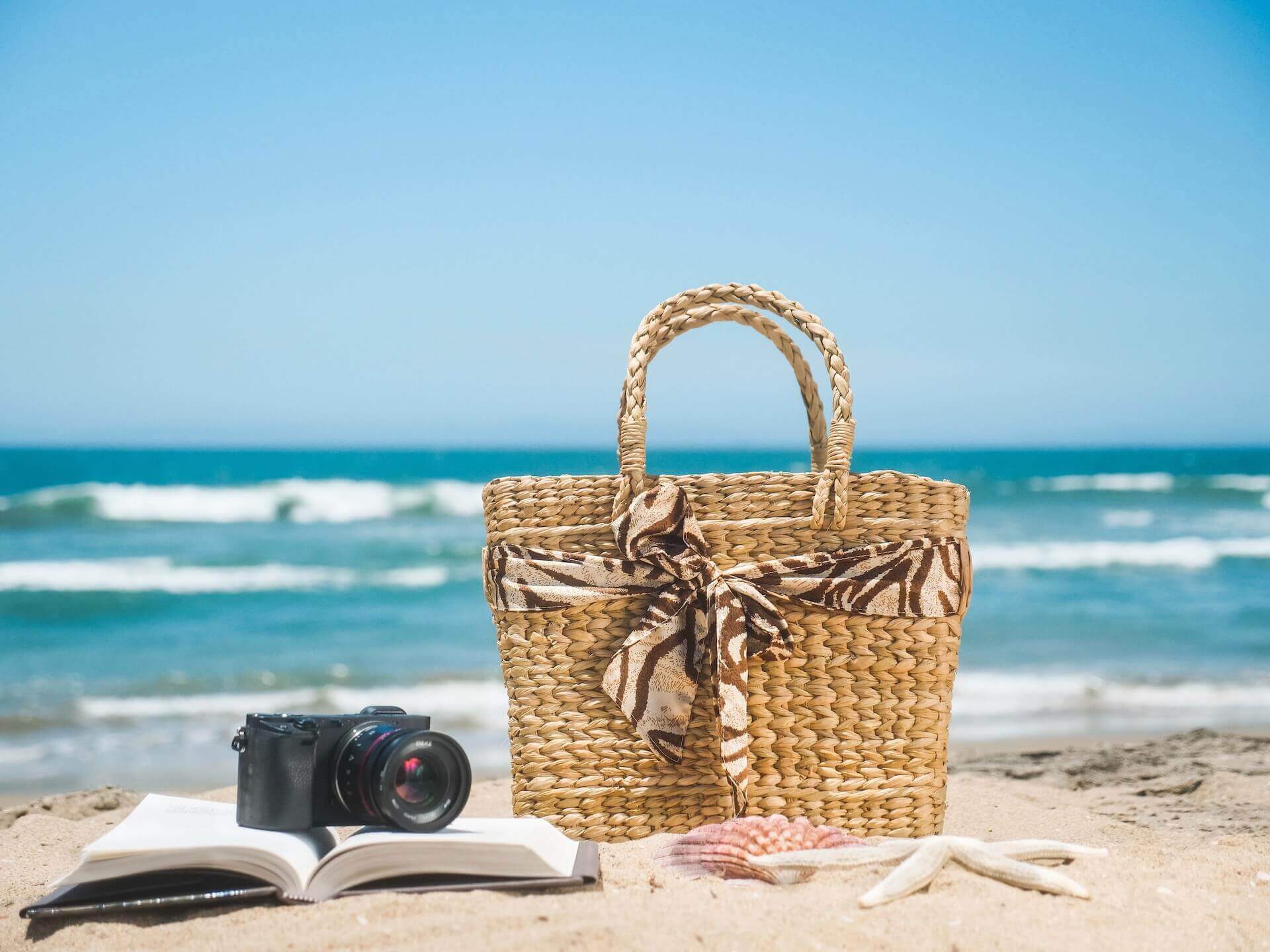 Beach bag and a book with a camera on the sand