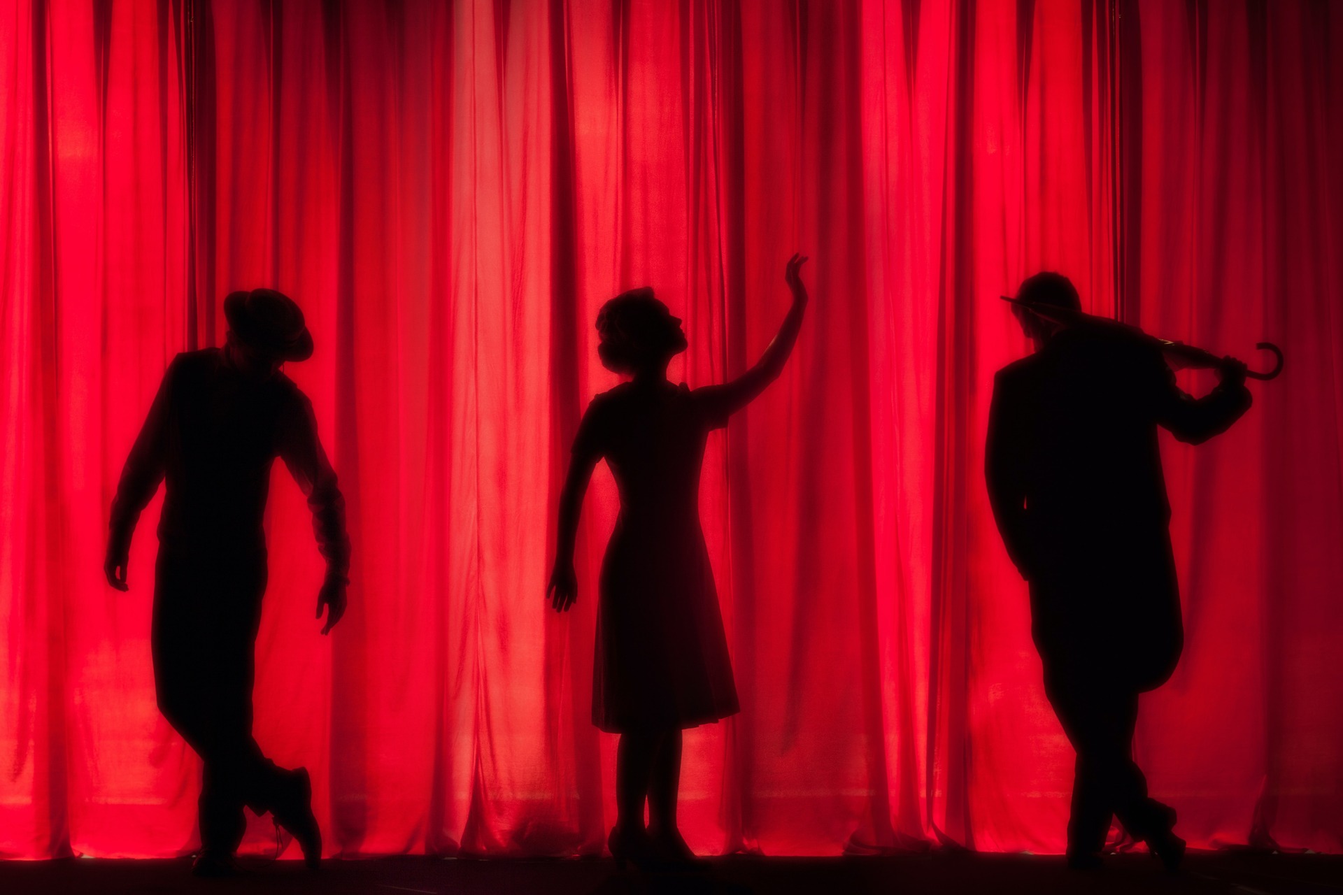 Three actors on stage in front of a red curtain