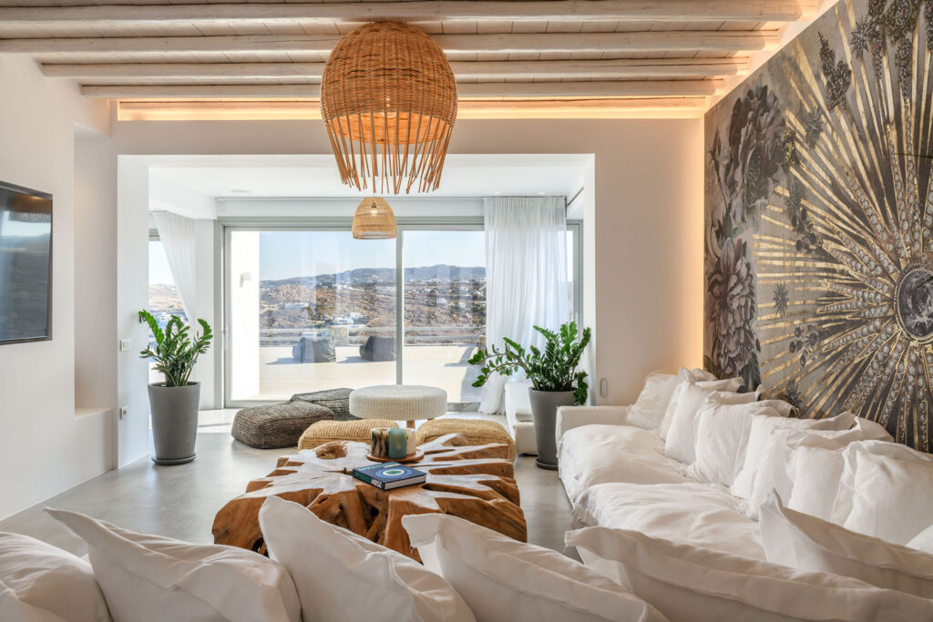 The indoor area of Mykonos villa with lounge chairs, a table and a view of the sea and the horizon.