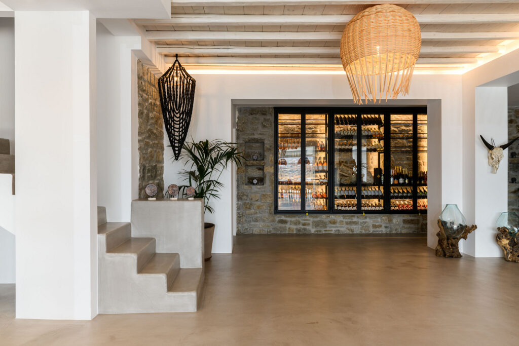 A stylish wine room with wine racks and a built-in bar in a Mykonos villa. The room features sleek wooden cabinetry and a wine refrigeration system, perfect for storing and enjoying a variety of wines. The ambiance is sophisticated and perfect for wine enthusiasts.