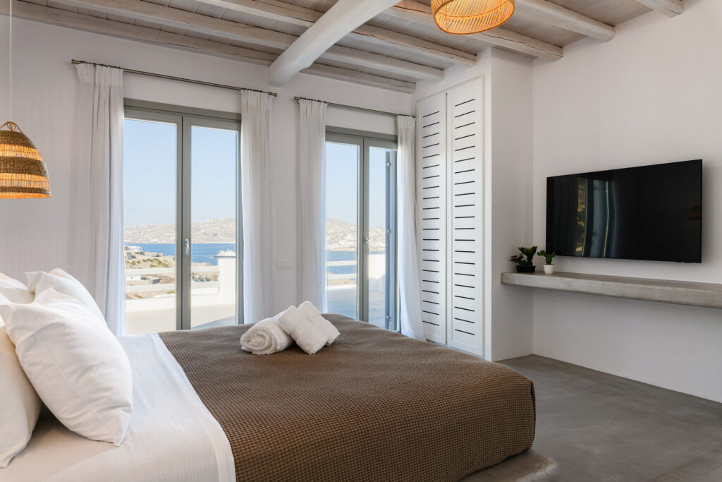 Indoor photo of a luxurious bedroom with sea view at Mykonos Top Villa, providing the ultimate vacation experience with stunning views and unparalleled comfort.