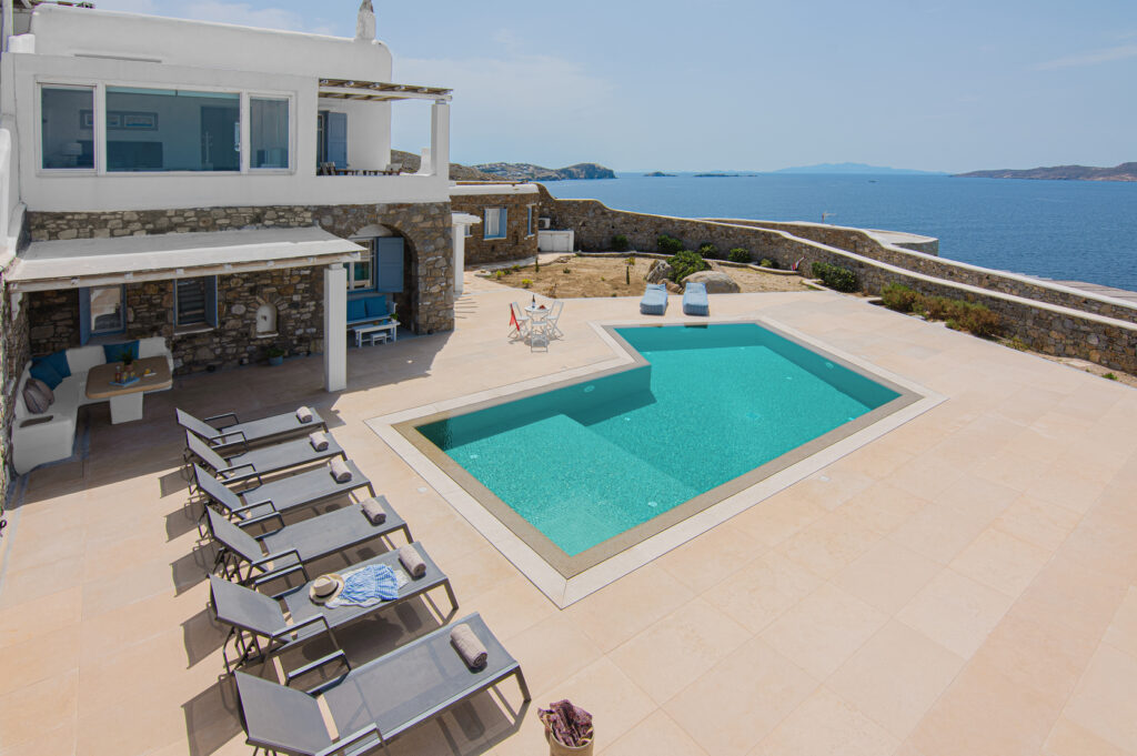 A luxurious outdoor area featuring a sparkling swimming pool with comfortable lounging chairs surrounded by lush greenery, inviting guests to relax and soak up the sun in Mykonos.