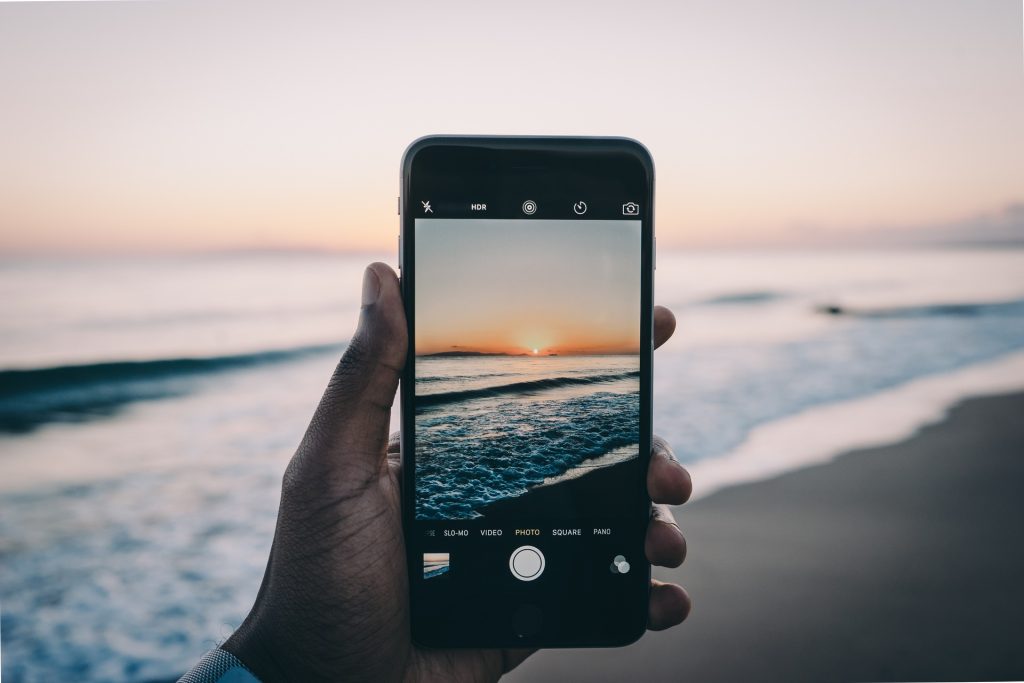 Man holding an iPhone in his hand and capturing a sunset