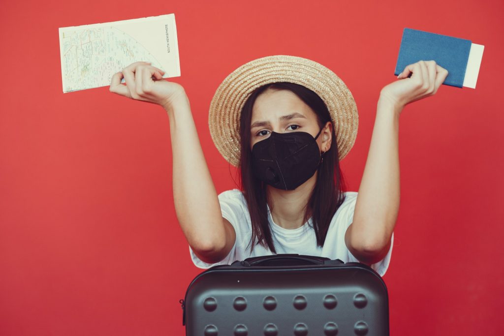 Woman with a face mask on, holding a passport and a travel map