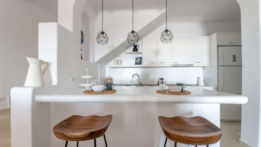 White and modern kitchen with wooden bar chairs in Mykonos secluded villa for rent.