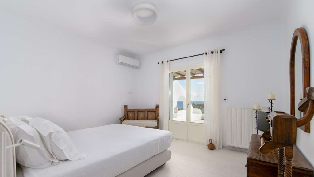 Single bed, white walls, and a wooden mirror in a bedroom of Mykonos finest villa for rent.