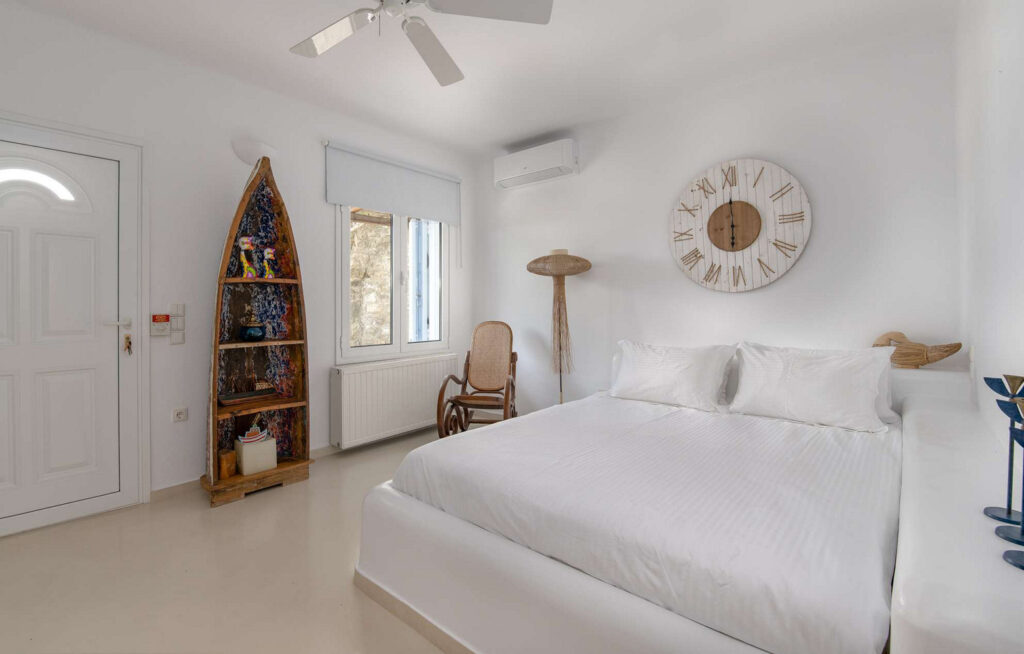 Wooden decor, comfortable bed, and white walls in a bedroom of Mykonos top villa for rent.