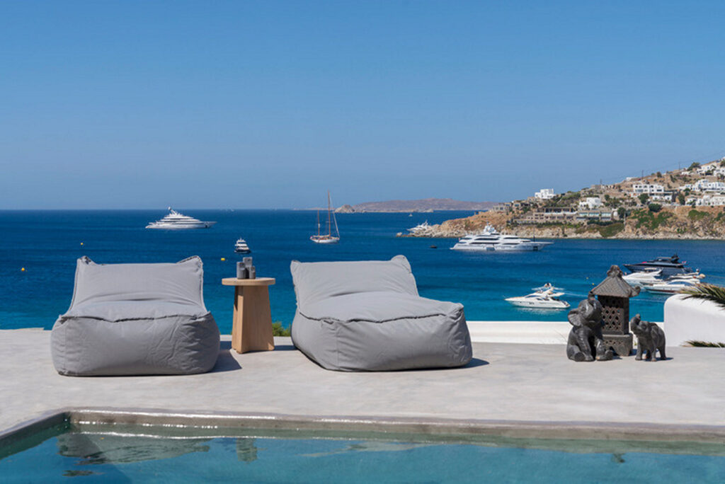 Cozy sun beds, a luxurious swimming pool, and a beautiful sea view from Mykonos' lavish rental villa.
