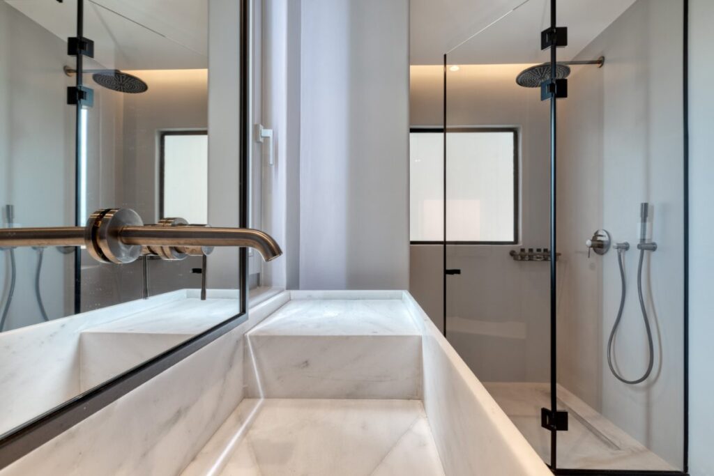 Glass, spacious shower, and marble sink in modern bathroom in Mykonos finest rental villa.