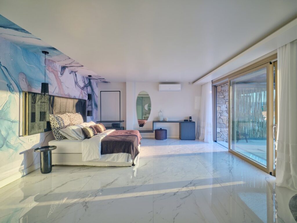 Colorful marble, comfortable bed, and large ceiling-floor windows in a rental vacation villa, Mykonos.