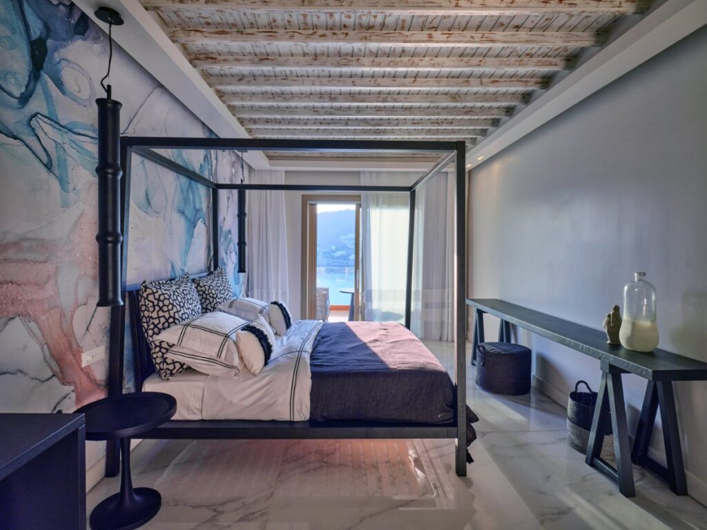 Cozy sleeping arrangements and artistically painted walls in a bedroom of a Mykonos lavish villa for rent.