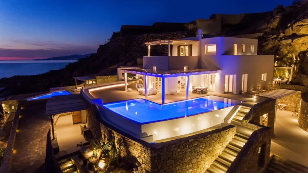 White luxurious villa in the night. Blue lights, infinity pool, and vibrant atmosphere in a private home for rent, Mykonos.