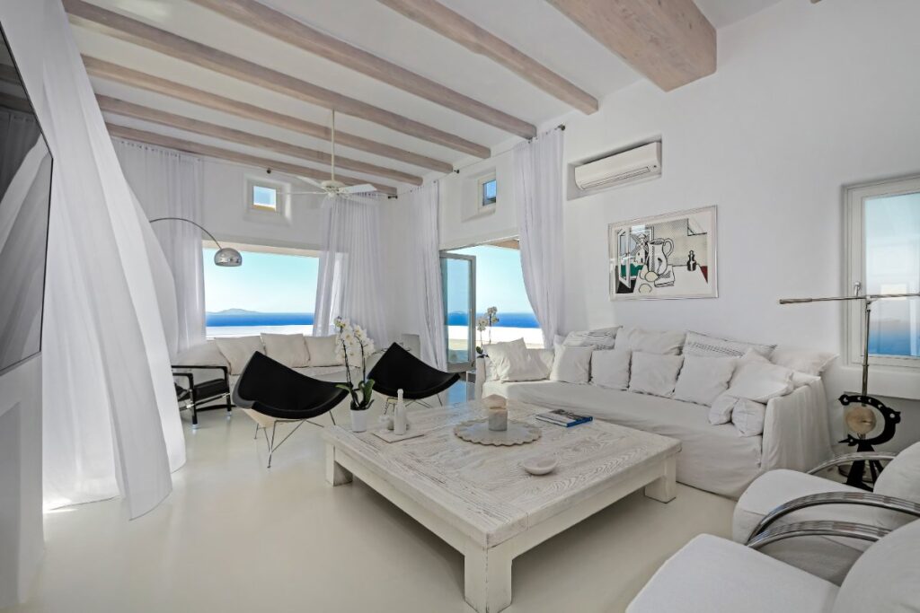 Black and white spacious living room, with high-quality furniture and breath-taking views of the blue sea and blue skies in a private home for rent, Mykonos.