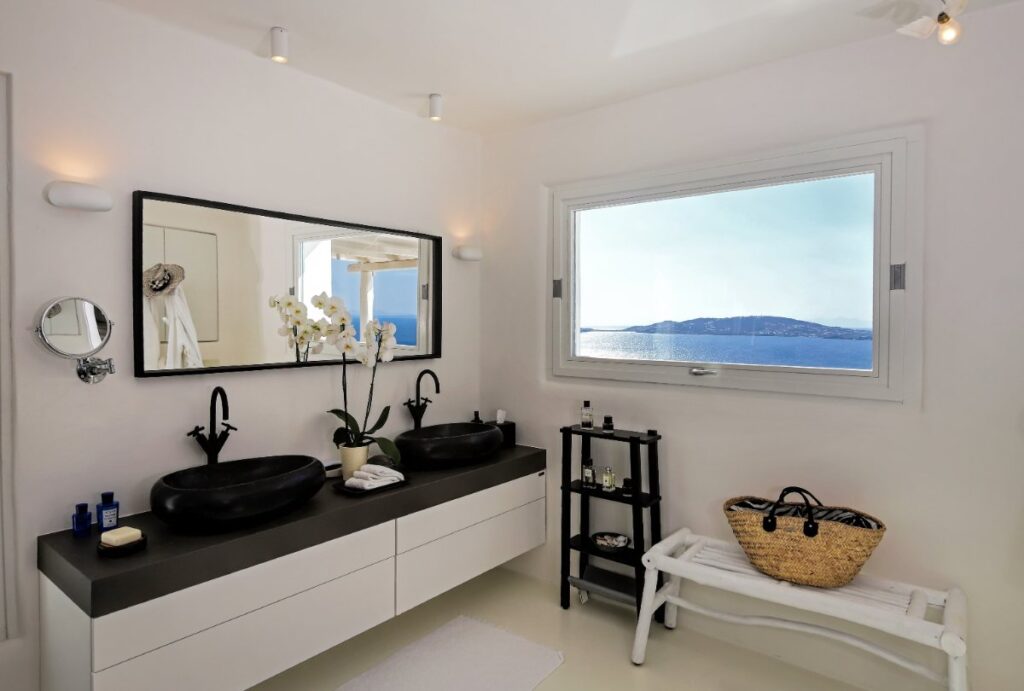 Elegant, full of bright bathrooms with a mirror and a wide waterfront window in the exceptional villa for rent in Mykonos, Greece.