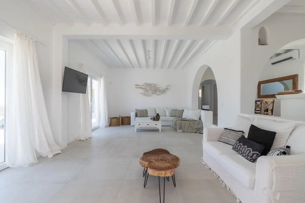 Splendid living room with high ceiling, white walls, and luxurious furniture in top Mykonos villa for rent.