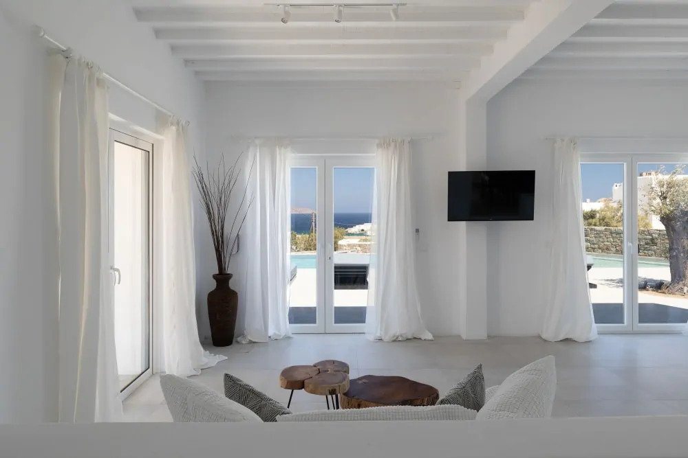 Soft color pillows, a white cozy sofa, and a wooden table set in the luxurious living room of Mykonos rental home