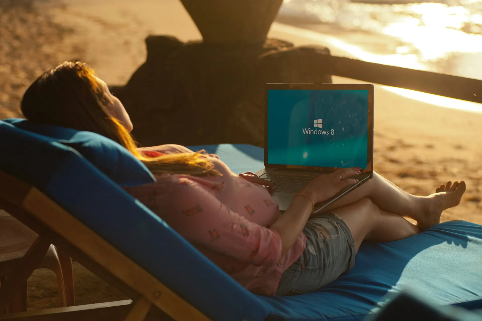 Woman working on her laptop while lying on a sunbed