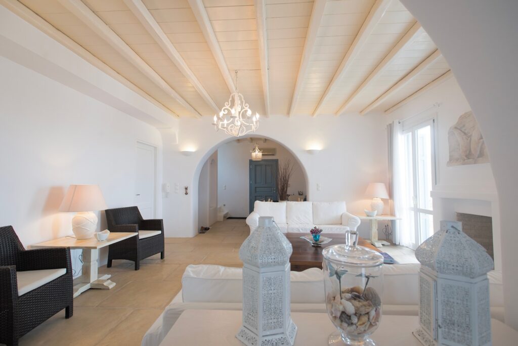 High ceiling, wooden details, and comfy furniture in the living room of Mykonos finest villa.
