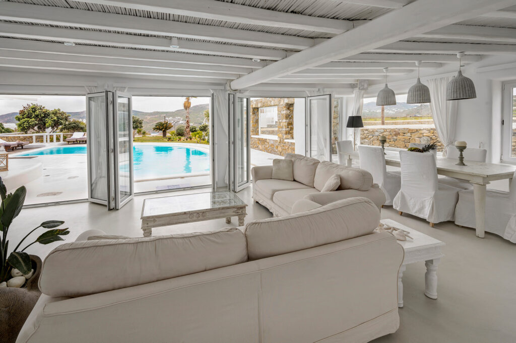 Spacious white living room with comfortable sofa and large windows, Mykonos rental home.