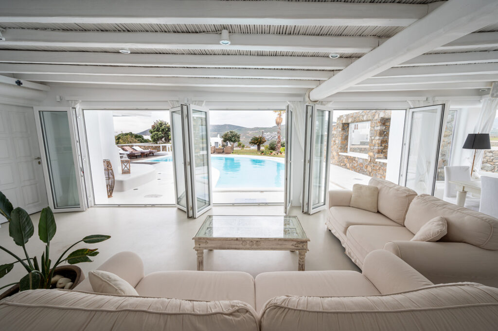 Large, cozy sofa, ceiling-to-floor windows, and private pool in Mykonos villa for rent.