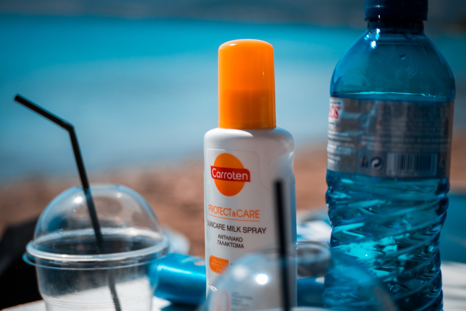 A bottle of sunscreen next to a bottle of water at the beach 