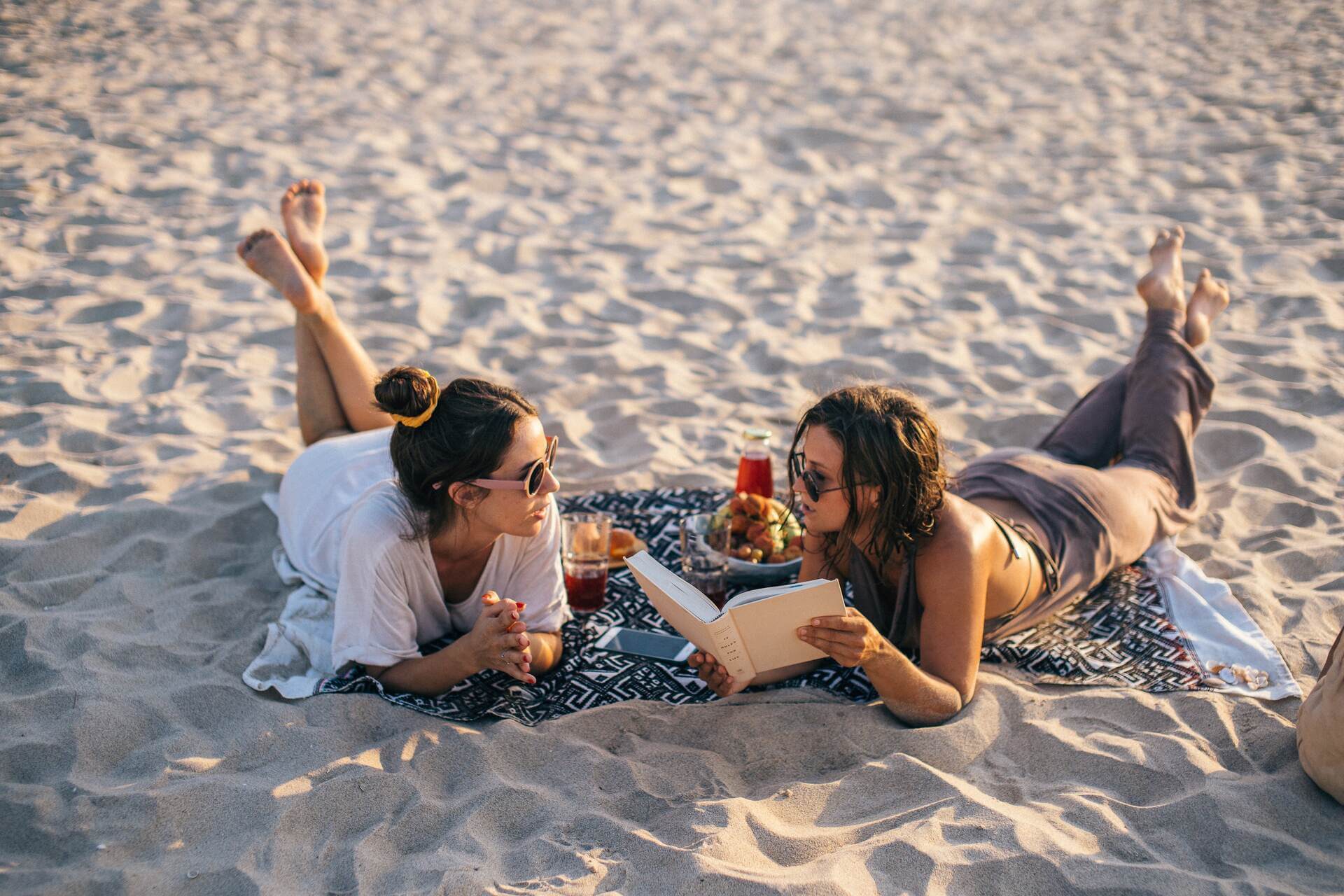 Women reading a book on a beach and talking
