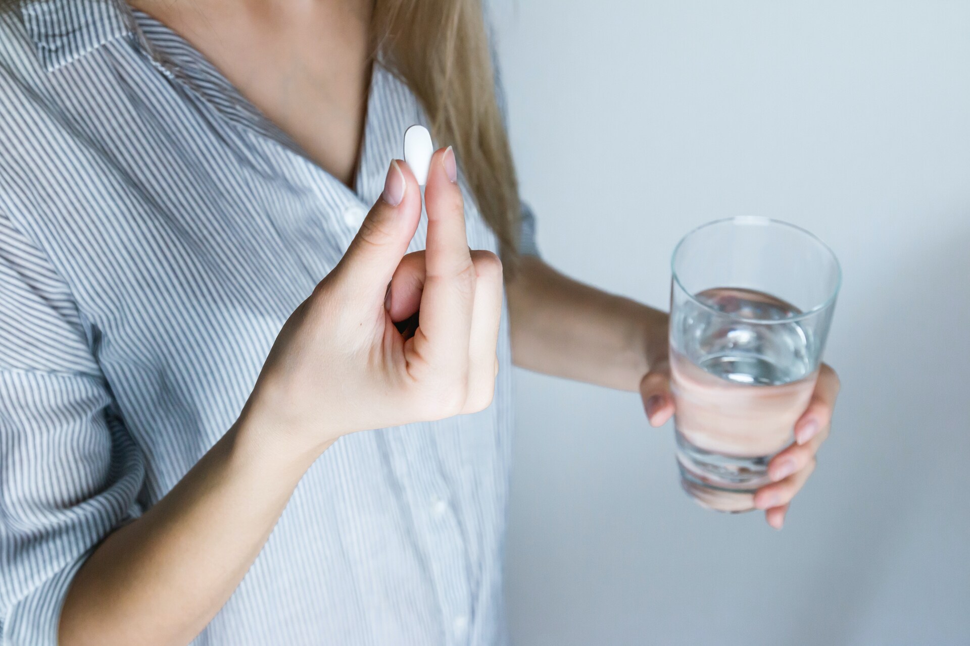 Woman holding a glass of water and a pill