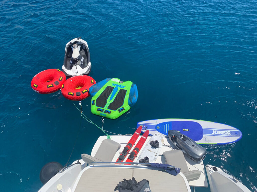 A jet ski, wakeboard, and towables next to a yacht

