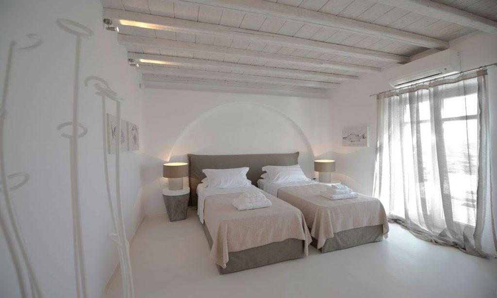 bedroom with beige sheets and separated beds with white wall