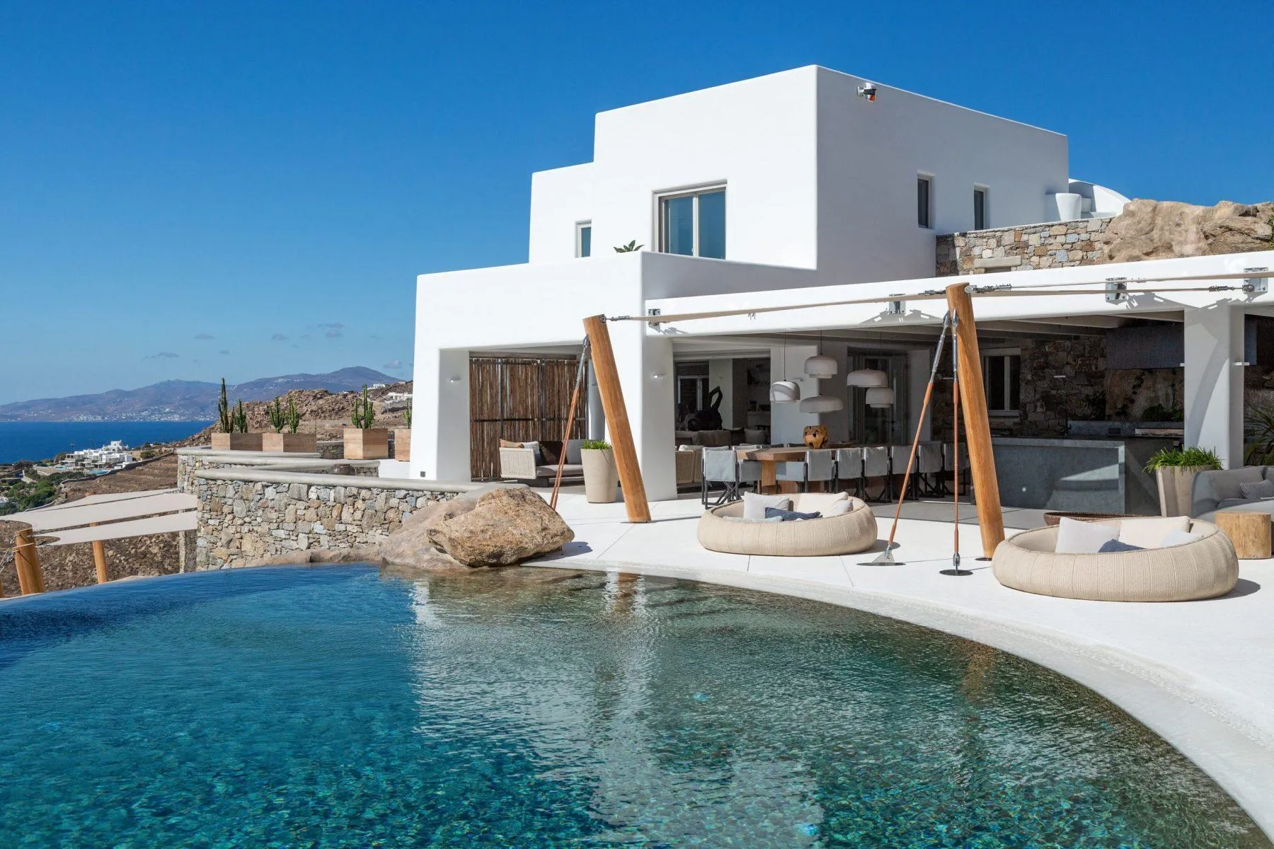 Pool with beds and a villa behind it, overlooking the coast of Mykonos