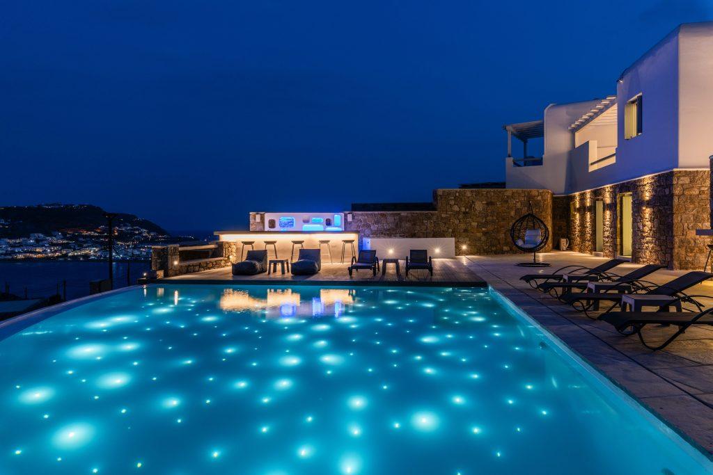 view of the starry sky and the illuminated city of Mykonos from the pool