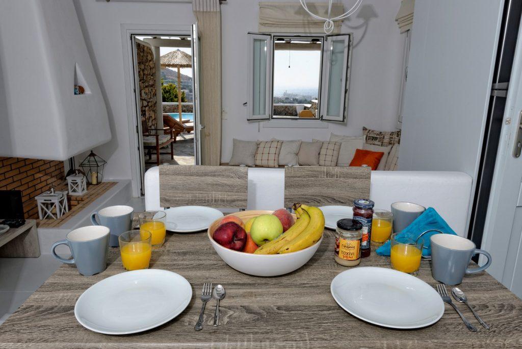 wooden breakfast table with bowl full of fruits and four orange juice glasses